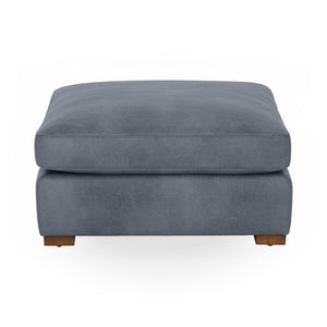 Classic Home Audrey upholstered ottoman with plush fabric and wooden legs, shown in a cozy living room setting.