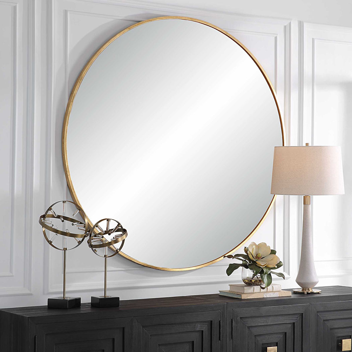 Uttermost Junius round wall mirror with a sleek, modern frame hanging on a wall, reflecting a stylish interior.