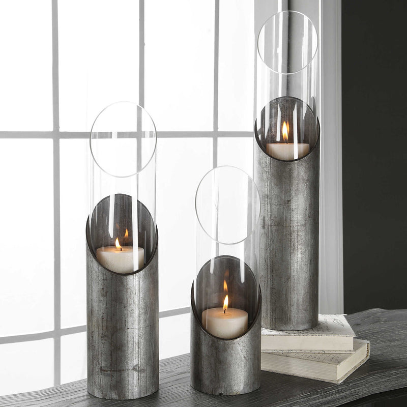 Set of three Uttermost Karter iron and glass candleholders in pearl silver and dark gray with candles inside.