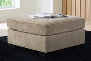 Benchcraft® Olten accent ottoman with a plush fabric surface and wooden legs, serving as versatile living room furniture.