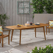 Outdoor Noble House Placidity expandable dining table with slatted tabletop and tapered legs, shown in a spacious outdoor setting.