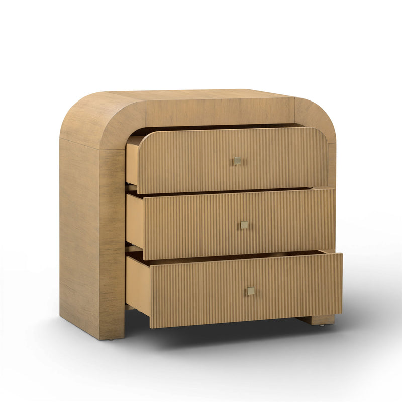 TOV Furniture Hump bedside chest with a sleek wooden finish and modern handles, positioned beside a bed in a contemporary bedroom.
