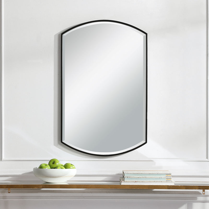 Black shield-shaped iron wall mirror by Uttermost, featuring a bold, decorative frame with a reflective glass center.