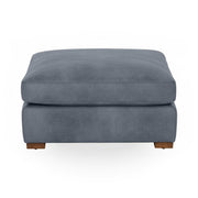 Classic Home Audrey upholstered ottoman with plush fabric and wooden legs, shown in a cozy living room setting.