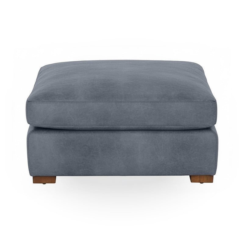 Classic Home Audrey upholstered ottoman with plush fabric and wooden legs, shown in a cozy living room setting.