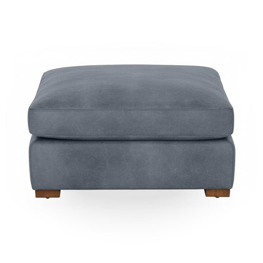 Classic Home Audrey upholstered ottoman with plush fabric and wooden legs, shown in a cozy living room setting.