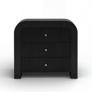 TOV Furniture Hump bedside chest with drawers, wooden finish, and modern design, placed beside a bed in a cozy bedroom setting.