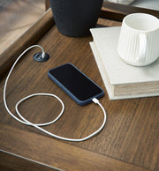 Brown Benchcraft Marxmore three-drawer nightstand with built-in charging station and modern design, placed beside a bed.