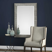 Uttermost Leiston metallic silver wall mirror with a sleek, modern frame mounted on a wall, reflecting light.