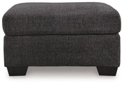 Benchcraft® upholstered ottoman from Loreo collection, featuring a plush, padded fabric top and sturdy wooden legs.