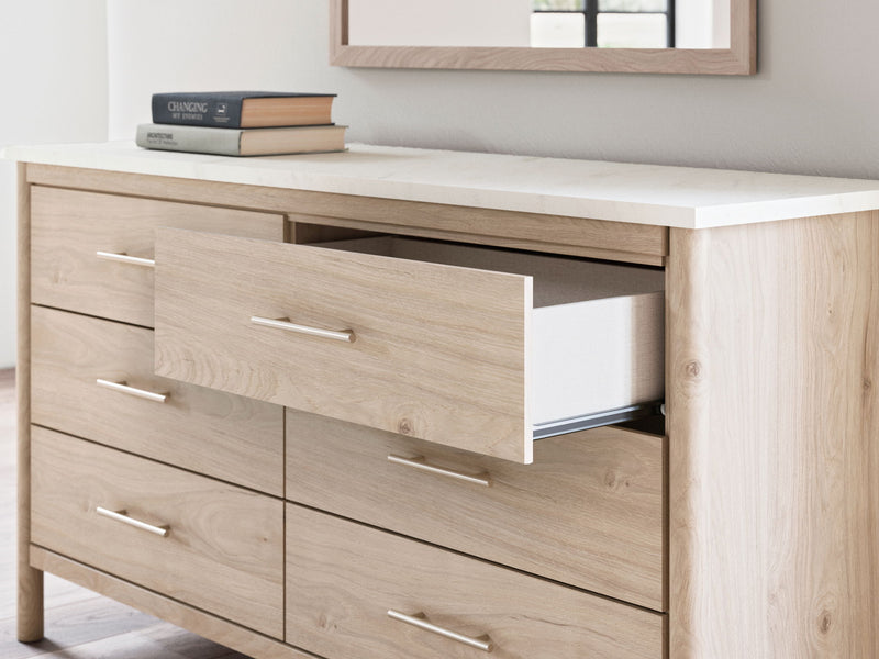 Signature Design by Ashley Cadmori six-drawer dresser with sleek wood finish and modern handles, standing on a light-colored floor.