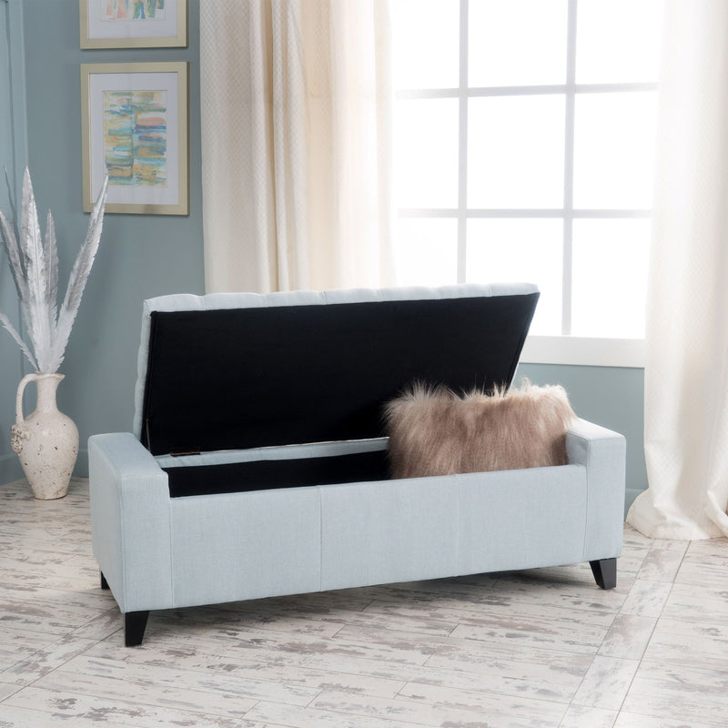 Noble House Guernsey storage ottoman with tufted top, beige fabric, and wooden legs, serving as a stylish storage solution.