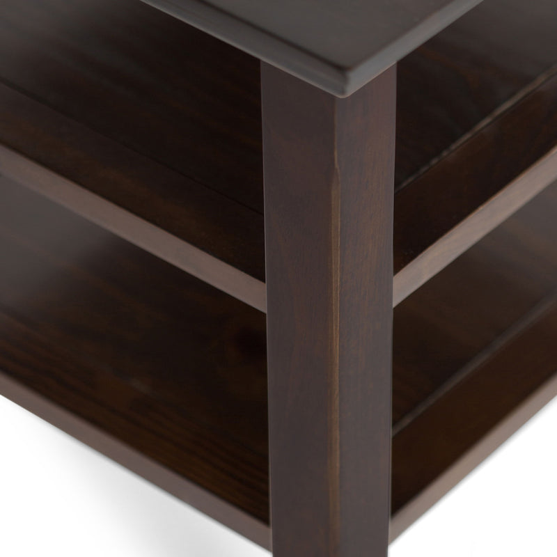 Handcrafted Acadian end table by Simpli-Home with wooden finish and simple design, placed beside a sofa in a living room setting.