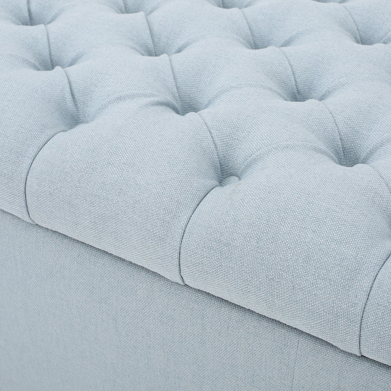 Noble House Guernsey storage ottoman with tufted top, beige fabric, and wooden legs, serving as a versatile ottoman and storage piece.