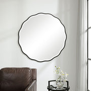 Uttermost Aneta round wall mirror with a sleek, modern frame hanging on a wall, reflecting a contemporary interior.