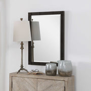 Aged black Gower vanity mirror by Uttermost with a sleek, modern design, reflecting in a stylish bedroom setting.