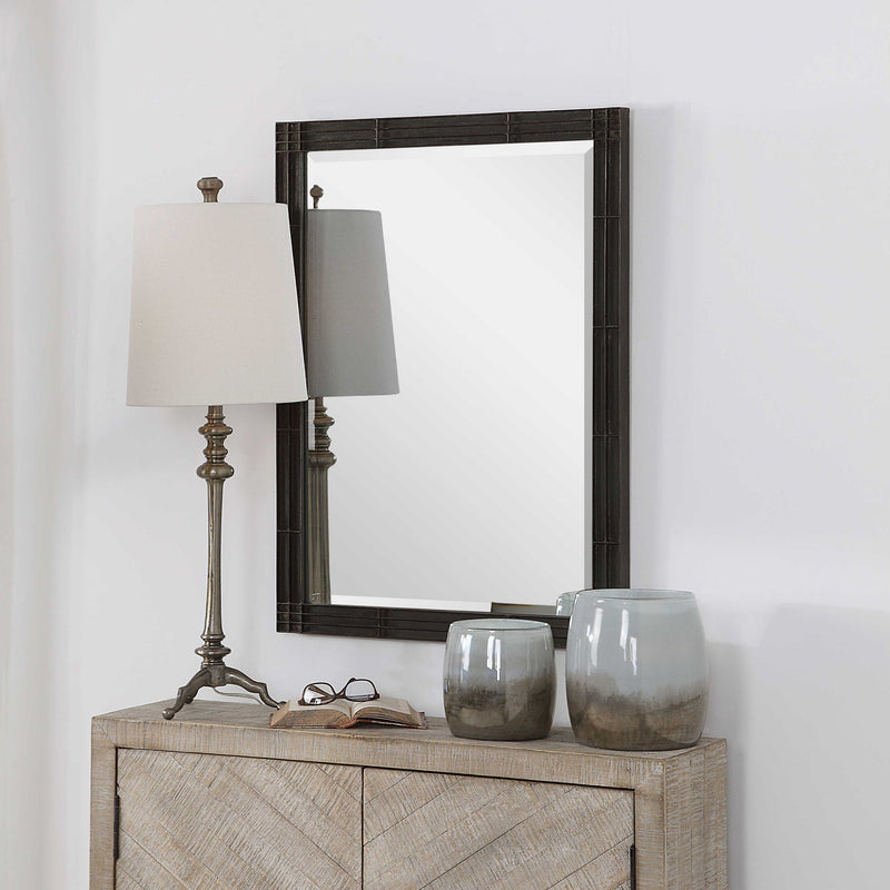 Aged black Gower vanity mirror by Uttermost with a sleek, modern design, reflecting in a stylish bedroom setting.