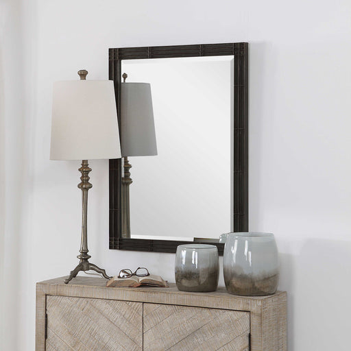 Aged black Gower vanity mirror by Uttermost with a sleek, modern design, reflecting in a stylish bedroom setting.