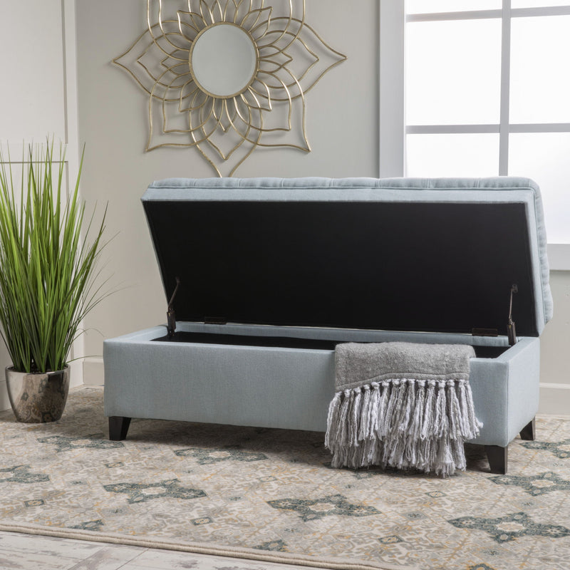 Noble House Juliana storage ottoman with birch wood legs, upholstered in neutral fabric, used as a footrest or extra seating.