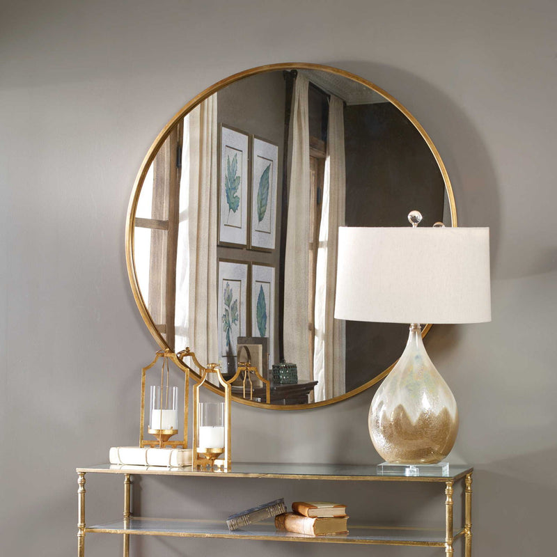 Uttermost Junius round wall mirror with a sleek frame, hanging on a wall, reflecting a modern interior space.