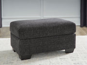 Upholstered Ottoman from Benchcraft® with a cushioned top and wooden legs, ideal for living room décor.