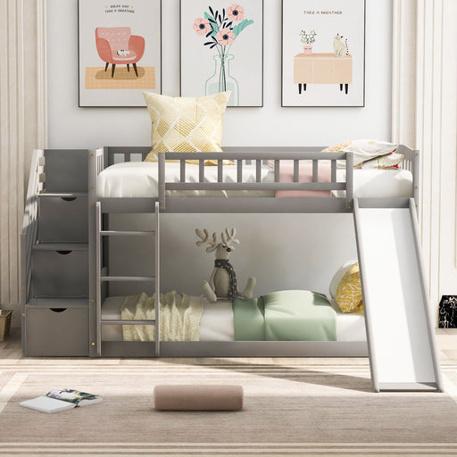 Gray DreamHaus twin over twin bunk bed with stairway, two drawers, and slide, featuring safety rails and a modern design.