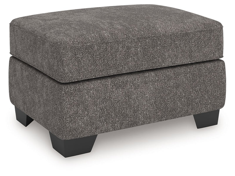 Benchcraft® Olten accent ottoman with a soft fabric surface and wooden legs, used as a versatile indoor footstool or side table.