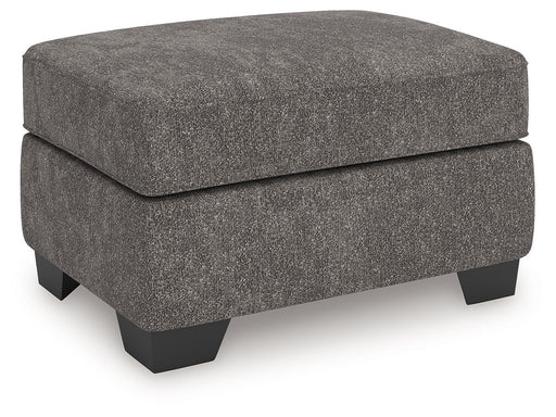 Benchcraft® Olten accent ottoman with a soft fabric surface and wooden legs, used as a versatile indoor footstool or side table.