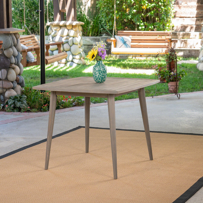 Modern Noble House indoor square dining table with acacia wood surface and toothpick-style legs.