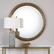 Uttermost Spera round gold wall mirror with a sleek, modern frame hanging on a wall.