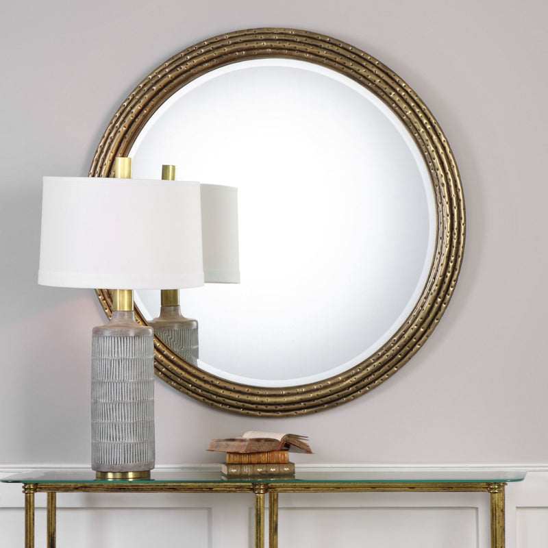 Uttermost Spera round gold wall mirror with a sleek, modern frame hanging on a wall.