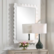 Uttermost Haya scalloped accent mirror with a decorative frame, hanging on a wall, showcasing elegant design and reflective glass.
