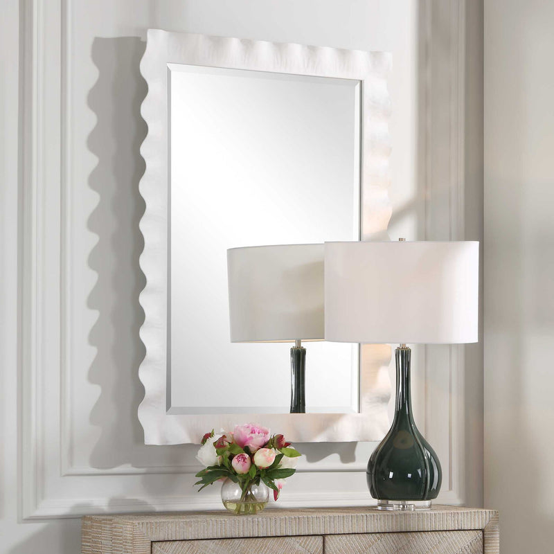 Uttermost Haya scalloped accent mirror with a decorative frame, hanging on a wall, showcasing elegant design and reflective glass.