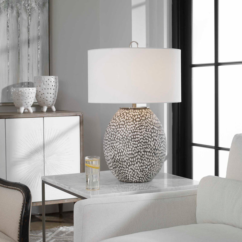 Uttermost Cyprien gray and white table lamp with a modern ceramic base and fabric shade, on a wooden surface.