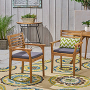 Set of two outdoor dining chairs with slat back design, gray fabric cushions, and acacia wood frames by Noble House.