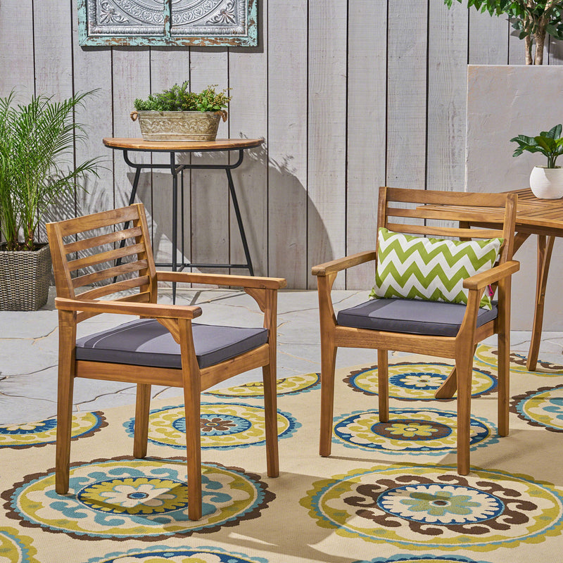 Set of two outdoor dining chairs with slat back design, gray fabric cushions, and acacia wood frames by Noble House.