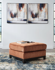 Ashley® Laylabrook oversized plush square accent ottoman in spice with dark wood trim, showcasing soft fabric and sturdy wooden legs.