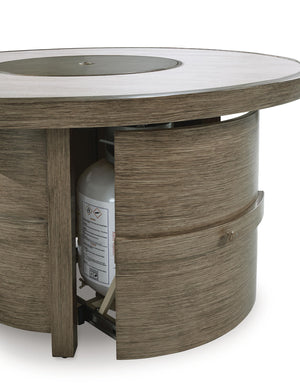 Beige round fire pit table from Rainier Ranch by Signature Design, featuring a smooth surface and sturdy metal base.