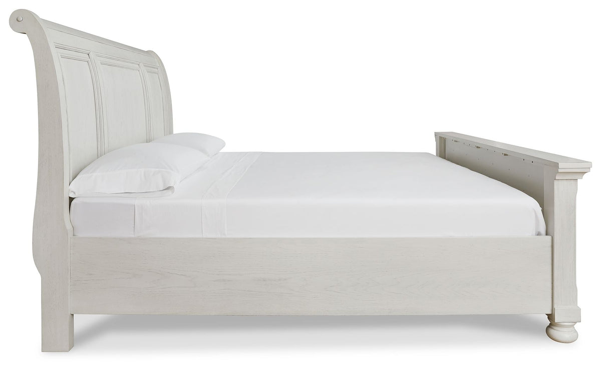 Robbinsdale Signature Design by Ashley storage sleigh bed with carved wood details and a dark finish, shown in a bedroom setting.