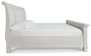 Robbinsdale Signature Design by Ashley storage sleigh bed with carved wood details and a dark finish, shown in a bedroom setting.