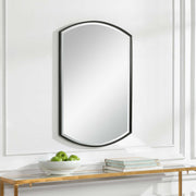 Black iron shield-shaped wall mirror by Uttermost with a bold, decorative frame reflecting a modern, artistic design.
