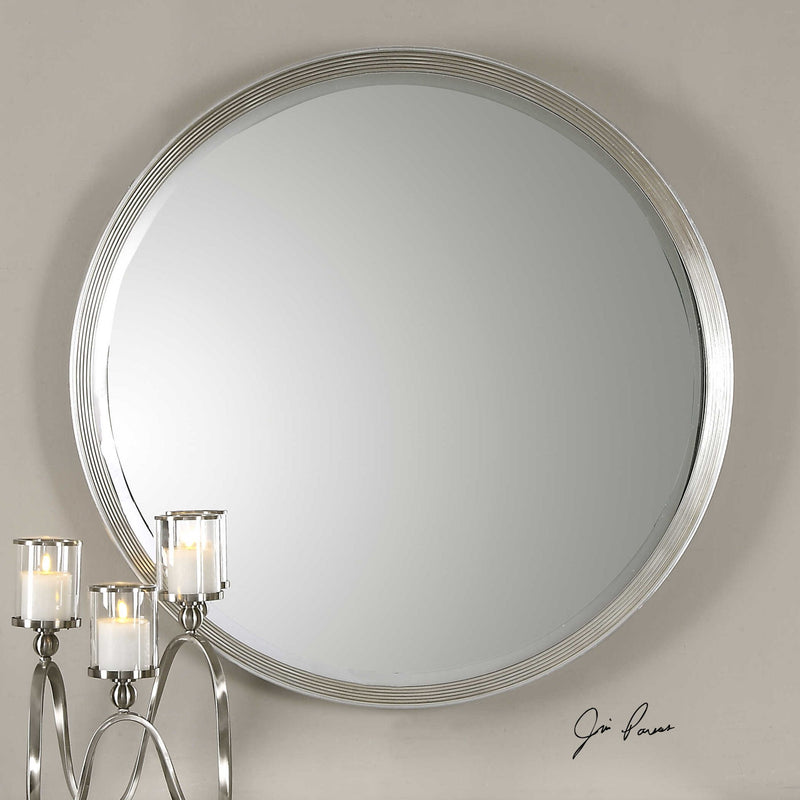 Uttermost Serenza round silver wall mirror with a sleek, modern frame, reflecting light in a contemporary interior setting.