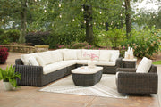 Signature Design Ashley Kimora 7-piece outdoor sectional with beige and dark brown cushions, including swivel glider, cocktail, and end tables.