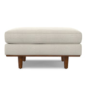 Simpli-Home Morrison handcrafted upholstered ottoman with cushioned top and wooden legs on a neutral background.