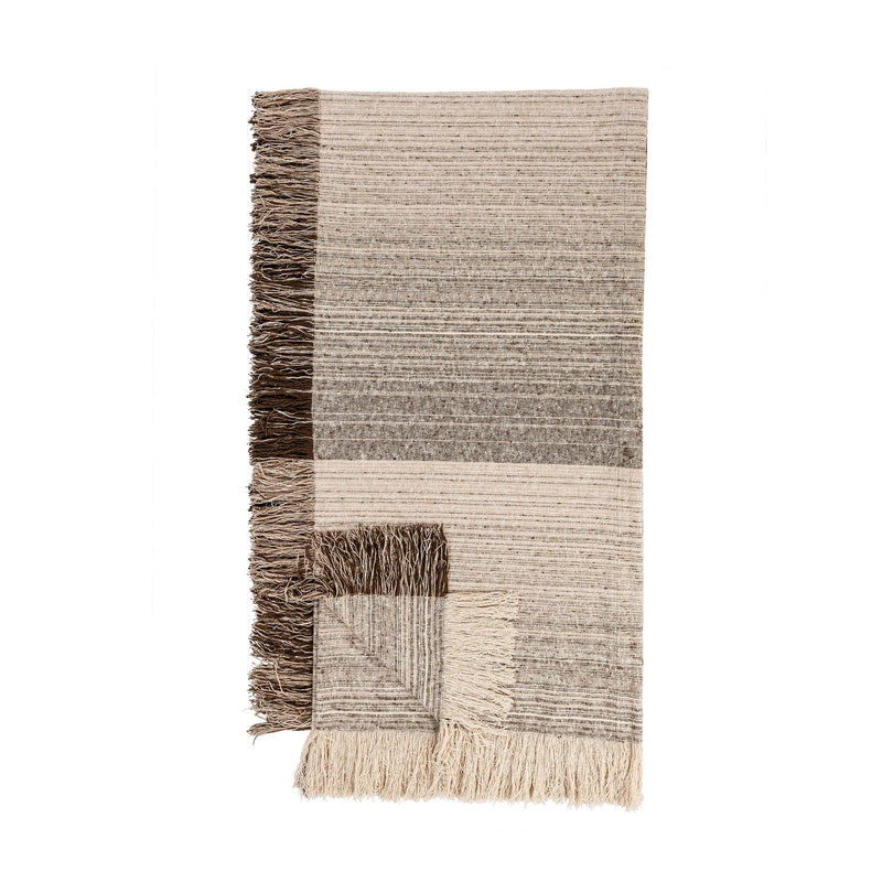 Soft beige Beryl blanket by Classic Home, shown draped over a cozy armchair with textured fabric and fringed edges.