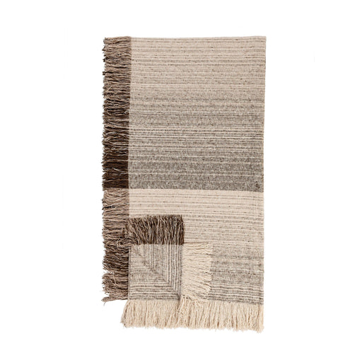 Soft beige Beryl blanket by Classic Home, shown draped over a cozy armchair with textured fabric and fringed edges.