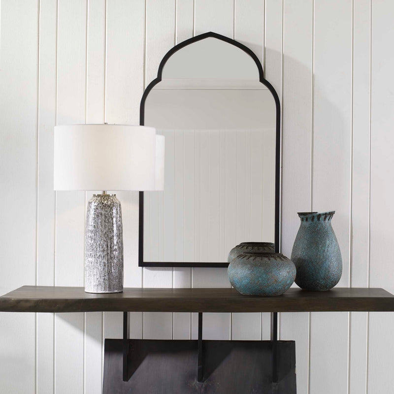 Uttermost Kenitra arched mirror with a sleek frame, hanging on a wall, showcasing its elegant design and reflective surface.