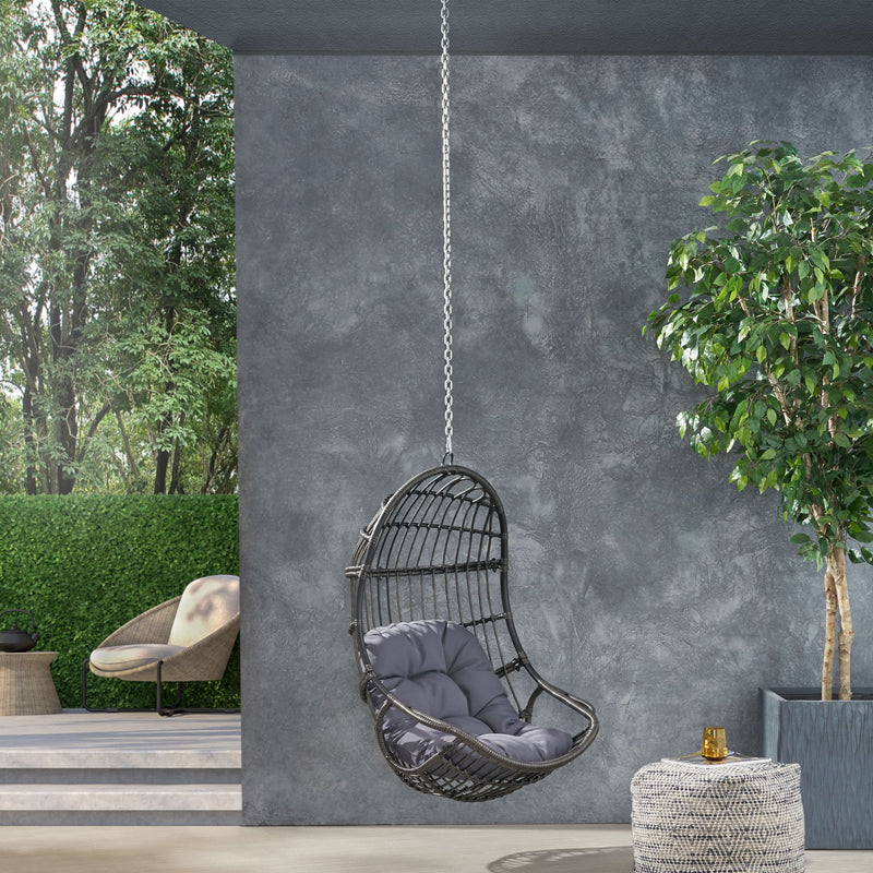 Rustic hanging basket chair with cushion by Noble House, featuring woven rattan design and cozy seating for indoor or outdoor use.