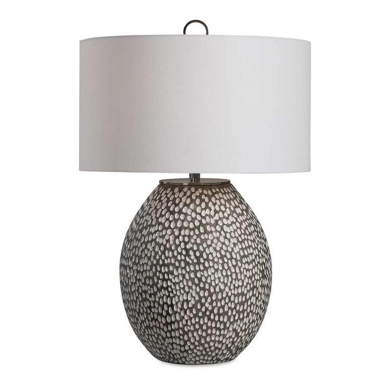 Uttermost Cyprien gray and white table lamp with a sleek, modern design and a cylindrical base on a wooden surface.