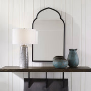 Uttermost Kenitra arched mirror with a sleek, curved frame, hanging on a wall, showcasing its elegant design and reflective surface.